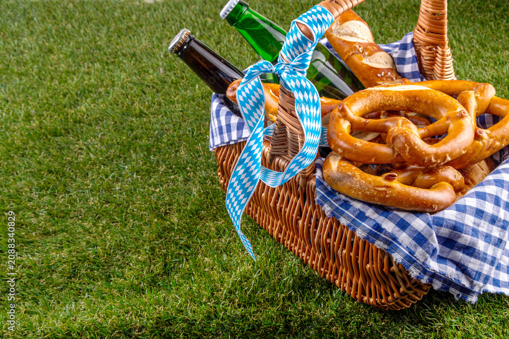 Fototapeta premium Oktoberfest picnic and barbecue food, bavarian party menu, bavarian sausages, pretzels, potato, sauerkraut, beer bottles, with picnic basket, checkered napkin tablecloth, Oktoberfest festive ribbon