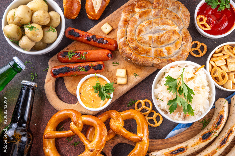 Fototapeta premium Oktoberfest picnic and barbecue food, bavarian party menu, bavarian sausages, pretzels, potato, sauerkraut, beer bottles, with picnic basket, checkered napkin tablecloth, Oktoberfest festive ribbon