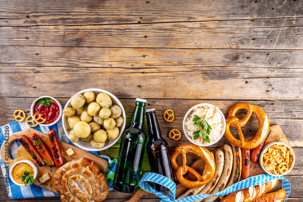 Fototapeta premium Oktoberfest picnic and barbecue food, bavarian party menu, bavarian sausages, pretzels, potato, sauerkraut, beer bottles, with picnic basket, checkered napkin tablecloth, Oktoberfest festive ribbon