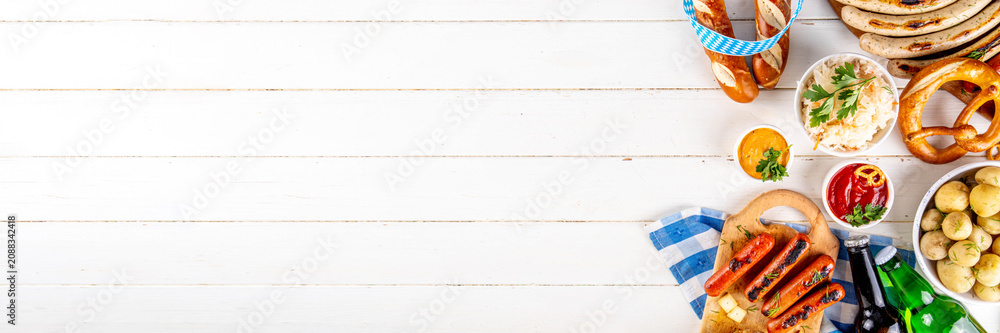 Fototapeta premium Oktoberfest picnic and barbecue food, bavarian party menu, bavarian sausages, pretzels, potato, sauerkraut, beer bottles, with picnic basket, checkered napkin tablecloth, Oktoberfest festive ribbon