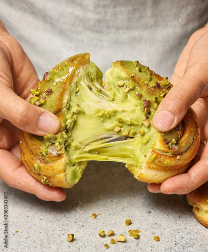 Close up of pistachio cream pastry being pulled apart with stretchy filling texture and crunchy nuts topping.