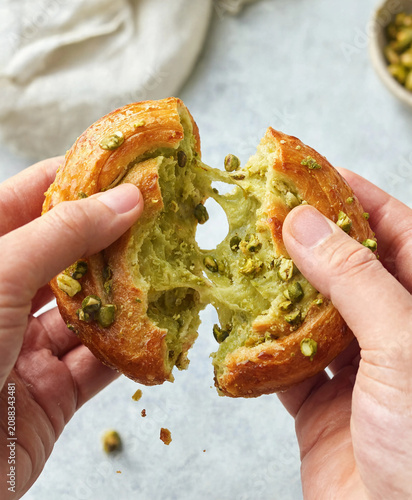 Close up of pistachio cream pastry being pulled apart with stretchy filling texture and crunchy nuts topping.