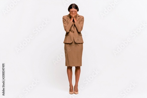 Businesswoman in brown suit standing and covering face with hands