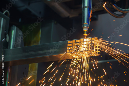 High-precision fiber laser cut machine performing an engraving and cutting process on a square steel pipe with sparkling light.