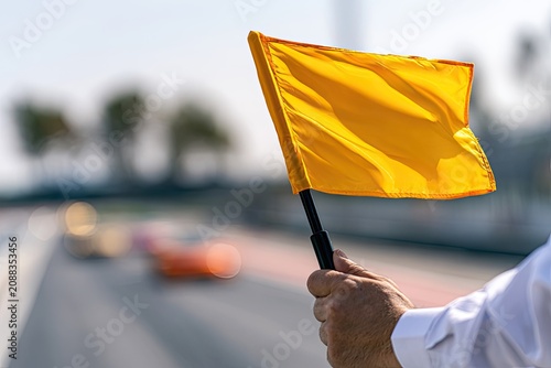 Hand waves bright yellow flag on a track, signaling warning to blurred vehicles