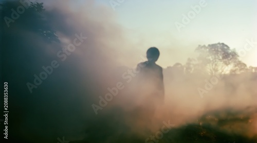 Figure emerges from thick smoke in a hazy, sunlit outdoor scene
