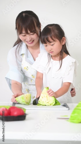 キッチンで料理を通してキャベツで包丁の使い方を学ぶ母親（親子）食育を実践する母親と小学生や幼児の女の子の縦動画