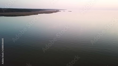 High forward drone clip above the Curonian Lagoon, its shores on the left, blue hour, Lithuania