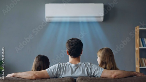 Family relaxing under cool airflow from modern air conditioner in living room