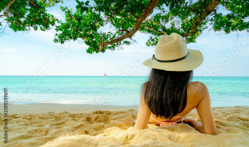 Photography Woman relaxing on tropical sandy beach beneath seaside tree while facing turquoise ocean