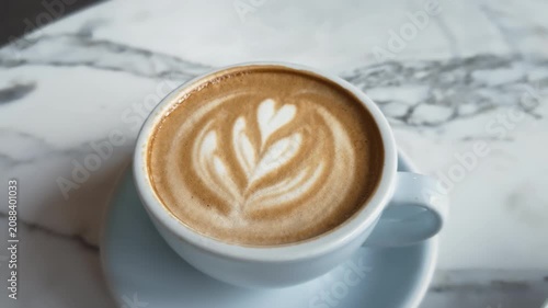 Fresh cup of cappuccino with latte art and plate of traditional Ukrainian cottage cheese pancakes syrnyky served with sour cream and berry jam on table in soft pastel light blue tones.