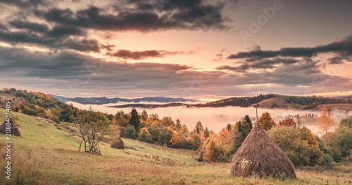 Breathtaking timelapse an autumn morning in Zakarpattia region of Ukraine. The sun rises over dramatic landscape, casting golden rays through heavy, moody clouds, while serene fog rolls through 