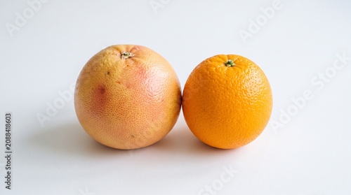 White plate with grapefruit whole and half deep pink interior, orange whole and half bright orange interior, plain white background emphasizing vivid contrast, symbolic representation of citrus variet