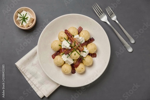 Bryndzove Halusky served with crispy bacon, topped with sour cream, garnished with rosemary. Concept of potato dumplings with sheep cheese bacon on grey surface.