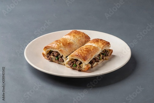 Kibinai on white plate, golden-brown rolled pastries revealing minced meat, onions, vegetables. Concept of savory pastries with minced meat onions pepper, culinary delight.
