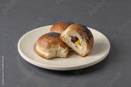 Kolace, fresh sweet buns with poppy seed cheese on white plate, one half eaten revealing creamy yolk, concept of warm flavors and comforting baked goods.