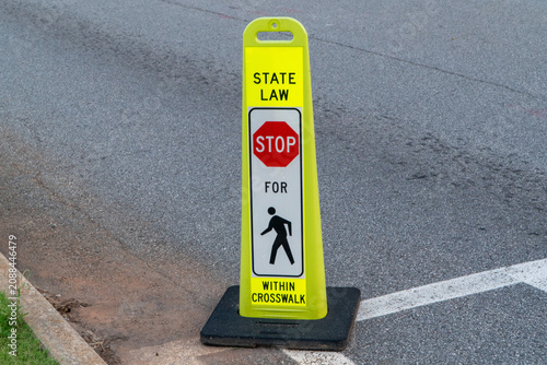 Foto Bright yellow A-frame sign instructing drivers to stop for pedestrians within crosswalks, emphasizing state law for enhanced road safety and traffic control on asphalt