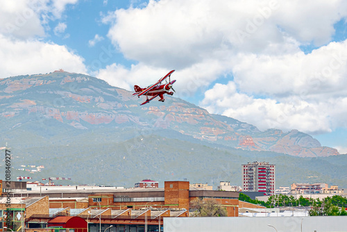A red aerobatic biplane performing air shows in a blue sky with white clouds. Classic airplanes