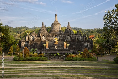 Foto Magnificent mini replica of Borobudur temple surrounded by lush gardens, pathways, and golden Buddha statues under a blue sky at Brahma Vihara Arama monastery in Bali