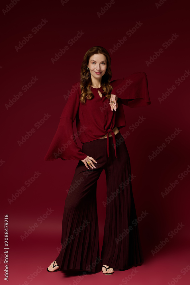 Fototapeta premium Stylish mature woman exuding elegance in a stunning maroon ensemble on a vibrant backdrop