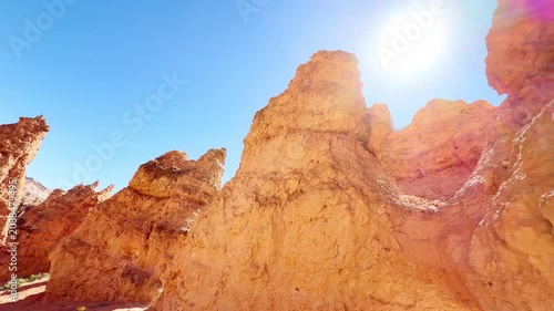 A smooth low angle cinematic shot looking up at surreal red sandstone peaks in Bryce Canyon, Utah. Majestic rock shapes under a bright sun and blue sky create an alien planet atmosphere. USA.