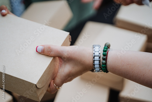 Obraz na płótnie Hands exchanging cardboard delivery box with wristwatch and green beaded bracele