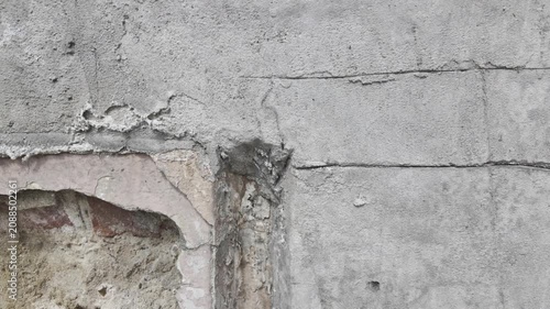 The camera pans diagonally from a damaged brick niche to a rough concrete stucco wall. 