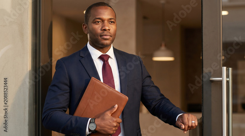 African American man in business suit entering office - Black man entering office building while carrying a leather portfolio  