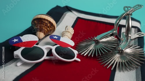 Still life with typical chilean cultural objects: spurs, poncho, spinning top, and flag sunglasses
