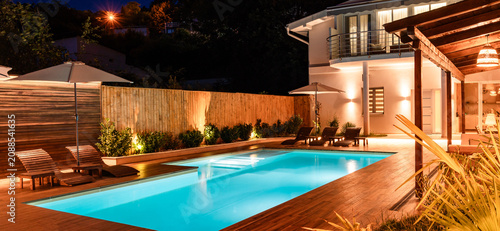 Foto Luxury backyard with illuminated swimming pool and modern house