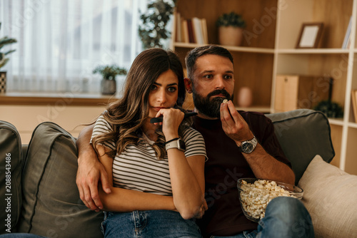 Fotografi Couple watching thrilling movie at home eating popcorn