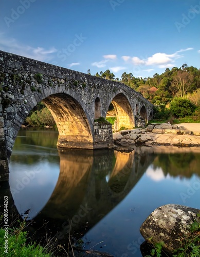 Historic Stone Arch Bridge Reflected in Calm River at Forest Edge