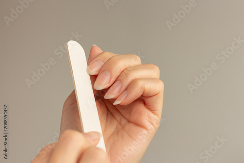Cuadro en lienzo Close-up of a young woman filing her natural fingernails with a nail file, showing the process of shaping natural long nails against a minimalist neutral beige background