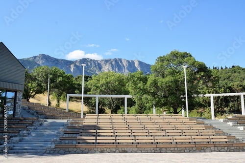 Empty wooden benches on a summer stage in a park with mountains in the background