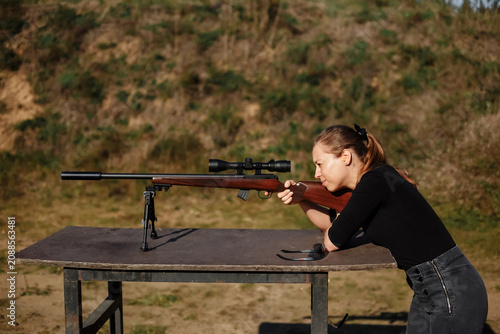 Fotografie Woman concentrating while aiming a scoped rifle on a bipod at an outdoor shootin