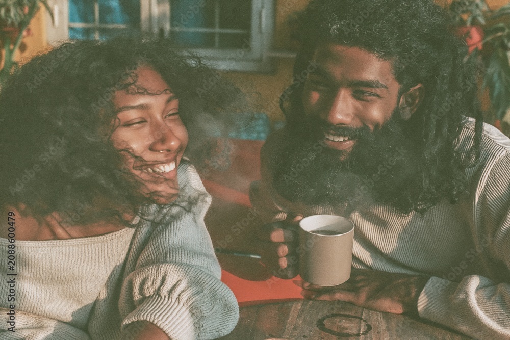 Fototapeta premium A happy young Indian couple laughing over coffee in a sunny home setting, featuring soft and film grain for lifestyle and leisure visuals