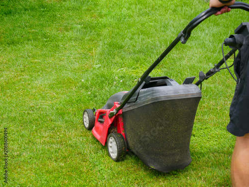 Man pushing lawn mower on green grass. Gardener cutting lawn in backyard. Professional landscaping equipment for home yard maintenance. Summer house chores and yardwork activity concept.