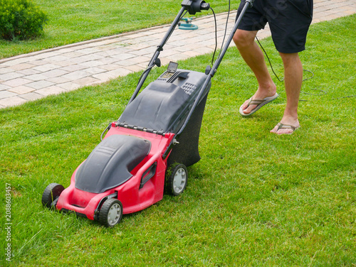 Man pushing lawn mower on green grass. Gardener cutting lawn in backyard. Professional landscaping equipment for home yard maintenance. Summer house chores and yardwork activity concept.