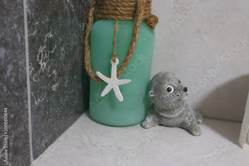 Decorative bathroom shelf featuring a frosted candle wrapped with natural rope and a starfish ornament beside a cute seal figurine
