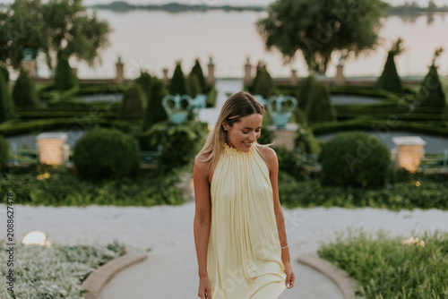 Woman walks through garden near water at dusk with green plants and trees