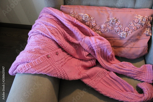 Pink shawl rests on a beige armchair beside a decorative pillow with floral patterns, creating a warm and inviting indoor atmosphere