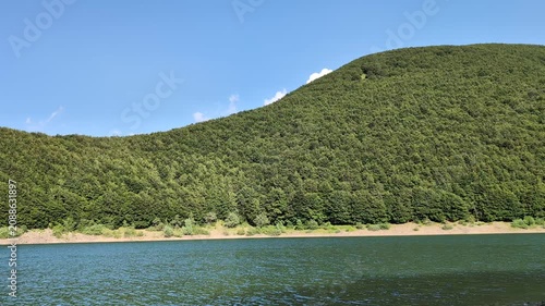 Mountain lake with gentle water ripples surrounded by green beech forest in the Apennines, Italy
