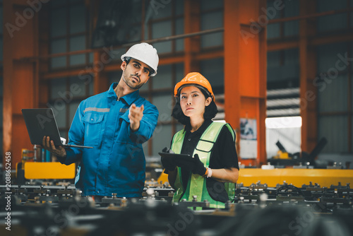 two professional engineer, worker, technician use clipboard discuss work, walk in steel metal manufacture factory plant industry. engineering man and woman wear hard hat check quality machine