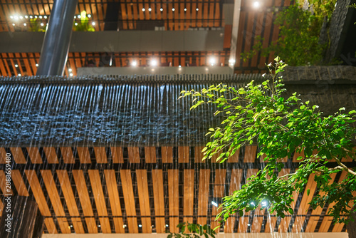 Foto A modern architectural structure featuring a cascading waterfall with water streaming down in front of wooden slatted panels arranged in a geometric pattern