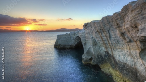 Morning light, sunrise, sun as a star, orange-red sky, dark blue calm sea, light blue sky, grey-blue clouds, tuff rocks, tuff rocks in the shade, Sarakiniko Beach, Milos Island, Cyclades, Greece