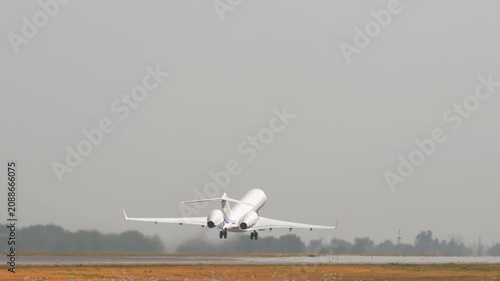 Private business jet taking off from airport runway and ascending into hazy sky, captured from behind with heat haze on tarmac, telephoto rear view