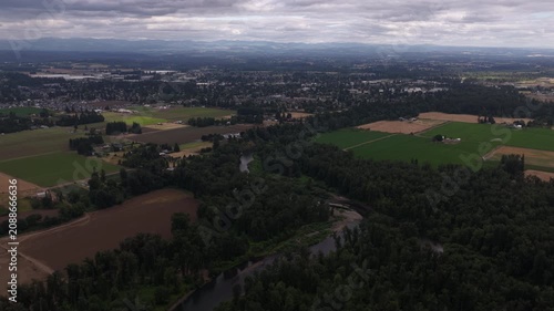 Aerial of river flowing through suburban and agricultural landscape near Canby Oregon with dense forest and green farmland