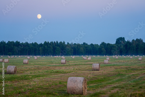 Hay Bales on Harvested Field Beneath Full Moon and Evening Sky in Peaceful Rural Summer Landscape Scene