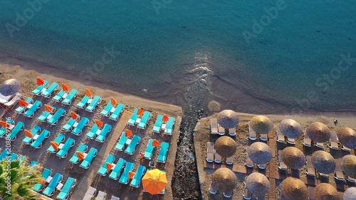A serene morning on Datça Beach with the contrast between turquoise sunbeds and straw umbrellas. Small thermal spring-fed stream meets the salty sea, merging the two waters