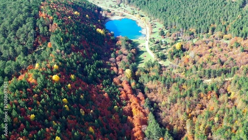 Colorful autumn forest revealing vivid blue pond nestled among red and green trees, Bolu, Turkey. Aerial forward flight